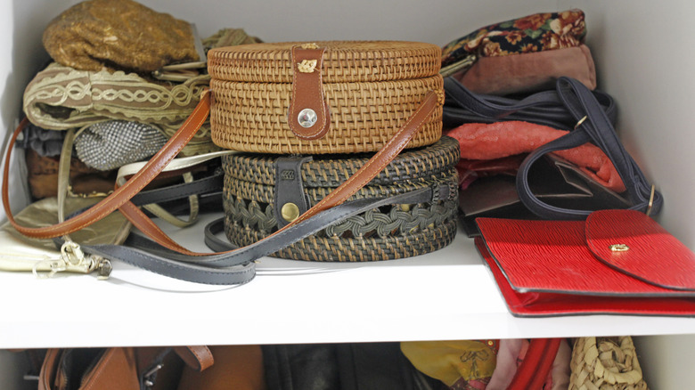 Handbags of various color and material, including vintage and woven, shoved in a closet in a pile