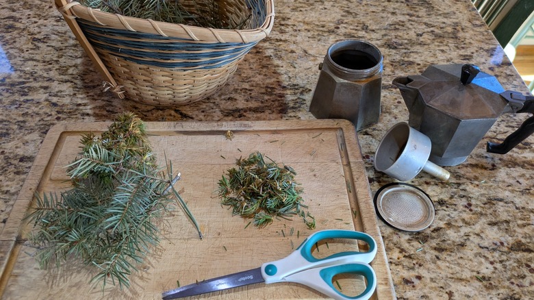 Chopped greenery cuttings on a wood board next to a separated moka pot