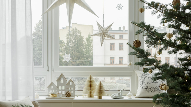 A window in a decorated room with a Christmas tree to one side and ornament hanging in front and sitting on the window ledge