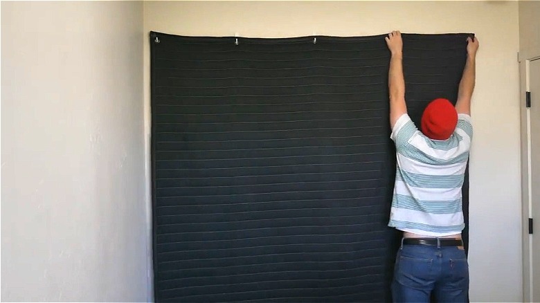 Man hanging moving blanket on wall for sound barrier