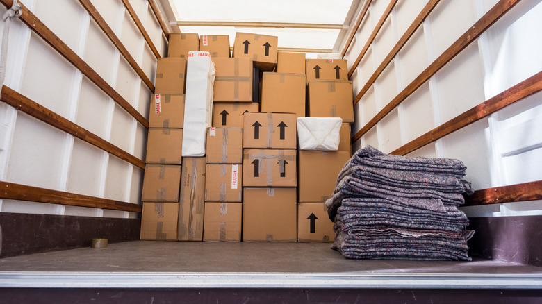 A stack of polyester moving blankets sit beside a number of stacked boxes inside a moving van.