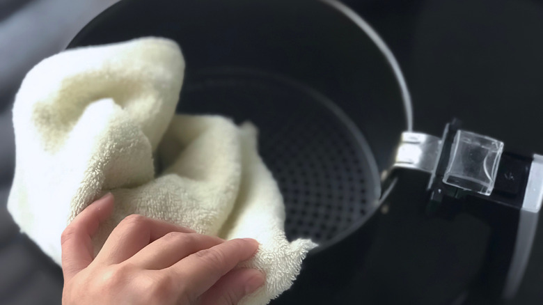 Person wiping air fryer basket with a soft towel.