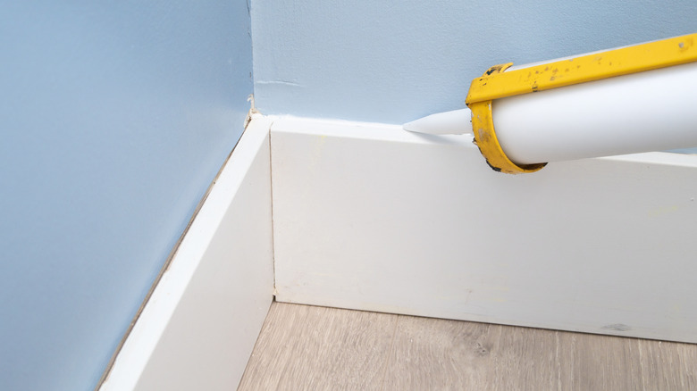 Close-up of a person re-caulking a baseboard