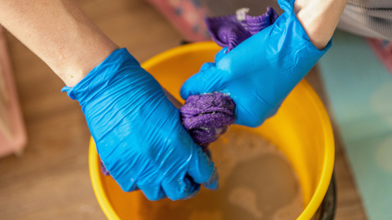 Close-up of a person wringing out a wet cloth over a bucket