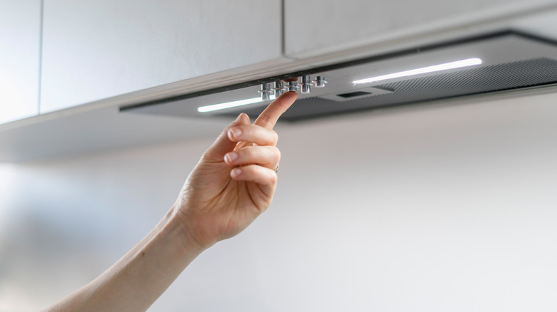 A hand pushing a button on an under cabinet range hood