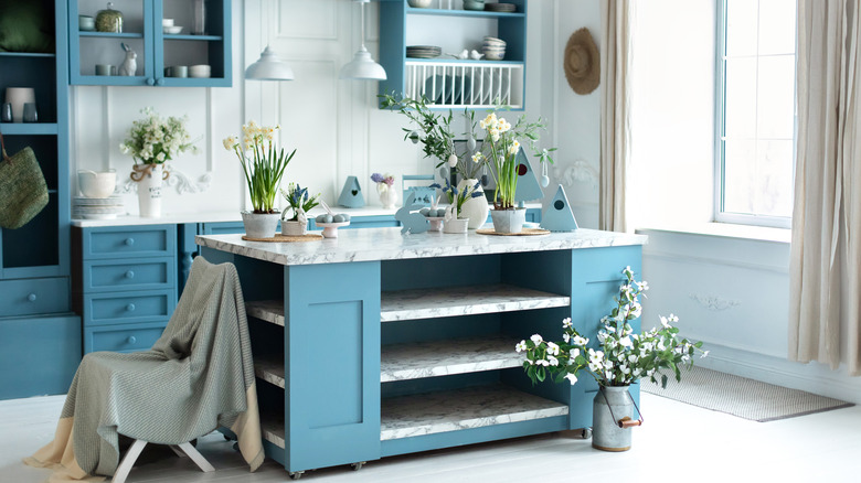 Sky blue kitchen with lots of flowers paired with white curtains and marble