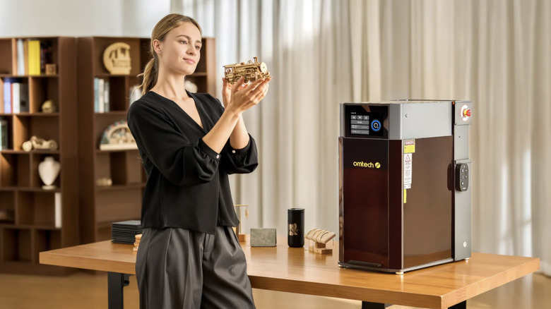 Woman looking at custom metal train creation while standing next to OMTech Solis Duo Dual Laser Engraver