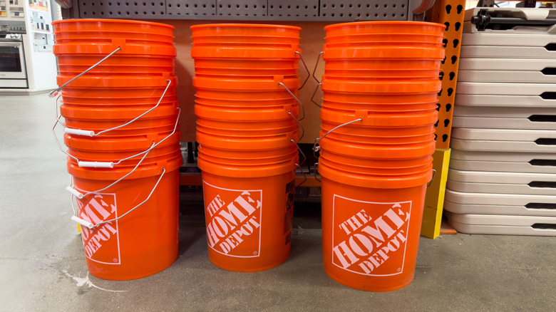 Three stacks of stuck orange 5-gallon buckets sitting on a concrete floor.