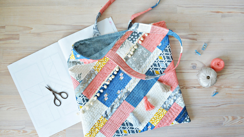 A colorful tote bag sitting on a wood surface with scissors, and yarn.