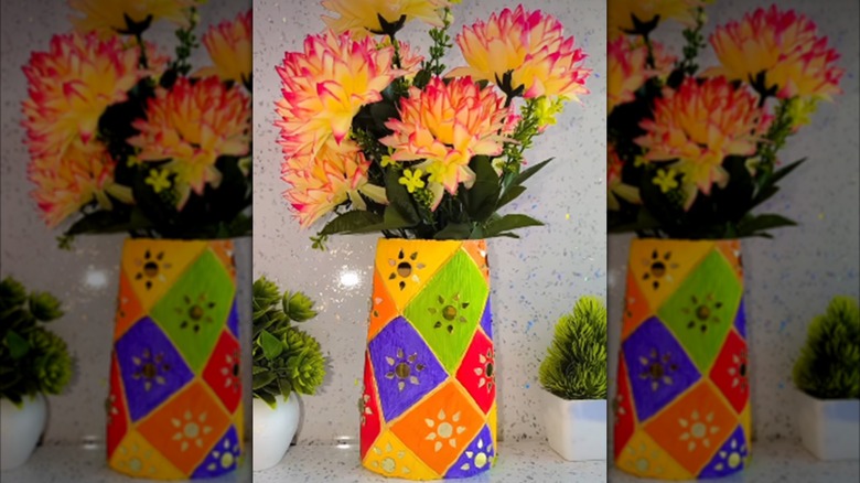 A countertop vase made of a painted shampoo bottle is filled with faux flowers.
