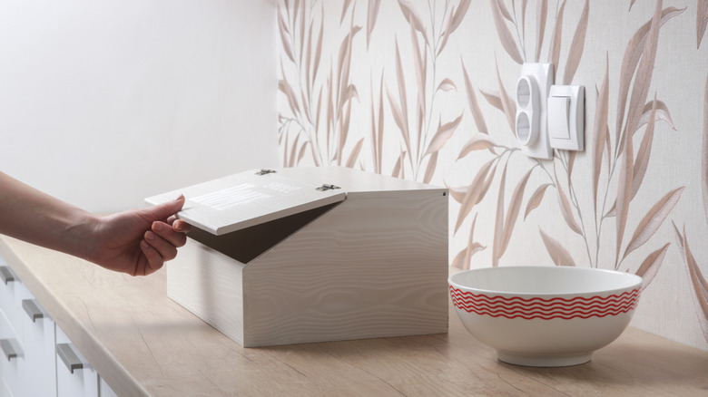 Person opening a bread box on a kitchen counter