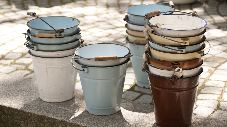 A collection of old colorful buckets sit on the side of the road.