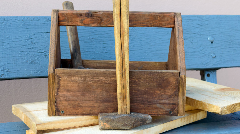 A vintage wooden toolbox with a hammer leaning on it with a blue bench.