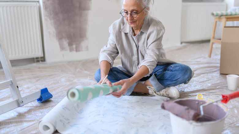A woman in a home in the middle of renovation unrolling wallpaper