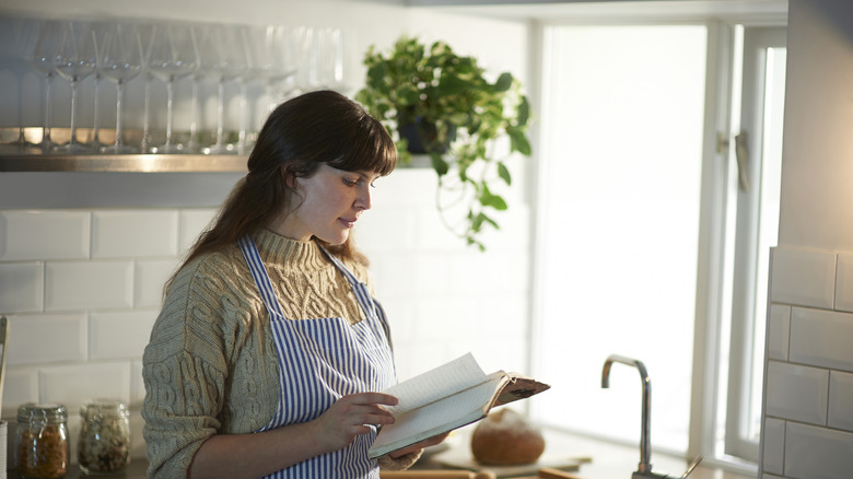 A woman holding a cookbook in her kitchen.