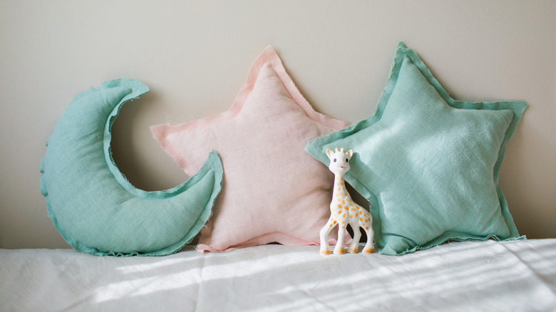 Pink and teal throw pillows shaped like stars and a crescent moon sit on a bed with a toy giraffe