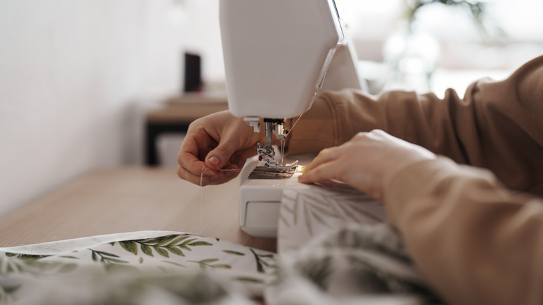 Close-up image of a person using a sewing a white and green patterned fabric using a sewing machine