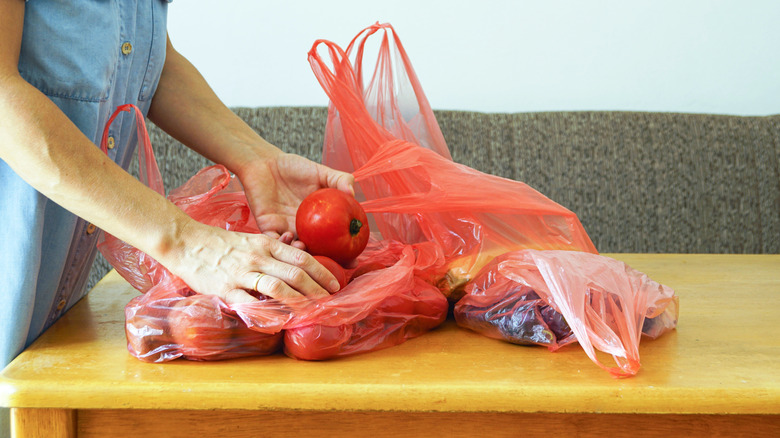 A person unloads groceries from plastic grocery bags