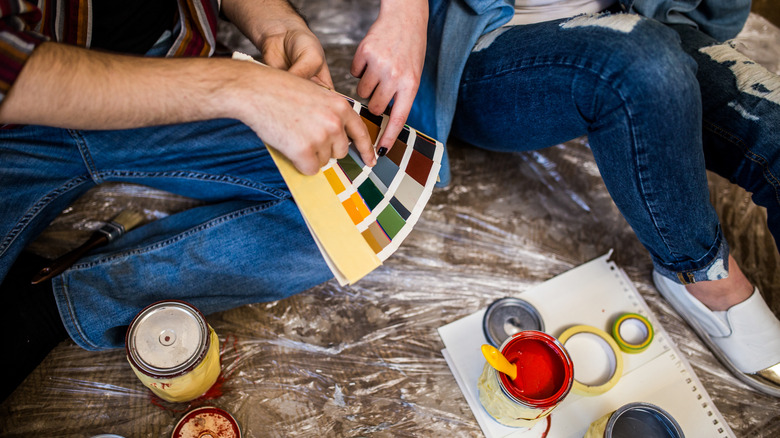 Two people are looking at color swatches, and some open paint cans sit in front of them.