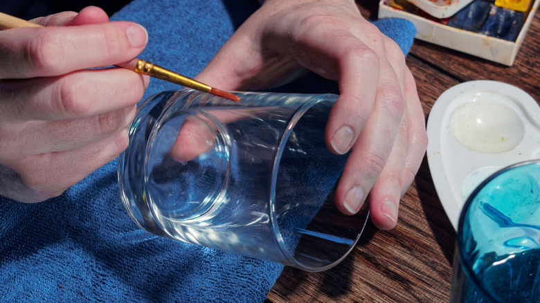 A person begins to paint a glass cup with a small paintbrush