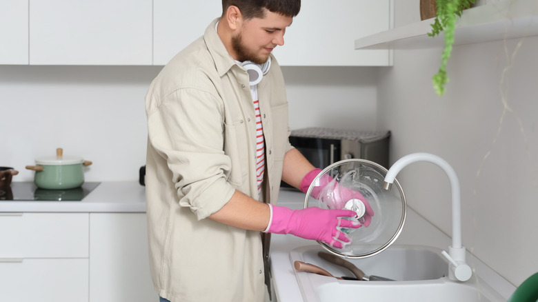 A person washes a glass pot lid in a kitchen sink