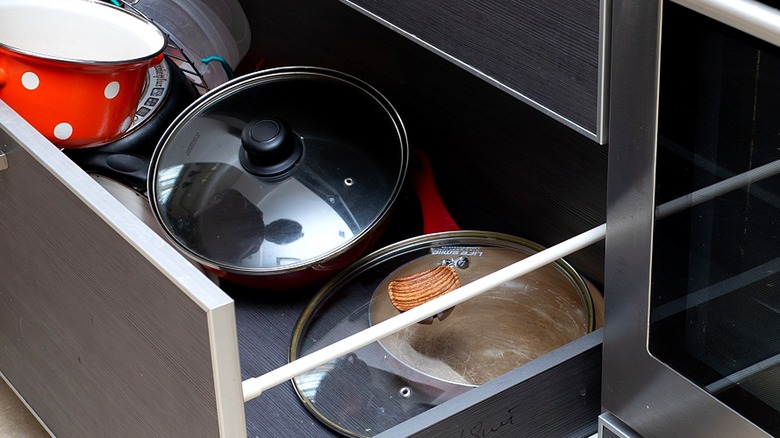 Close-up of a stove drawer with a red and white polka dot pot and pot or pan lids