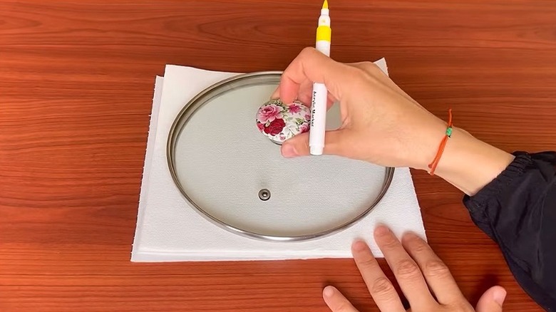 Close-up of a person's hands holding a yellow marker while holding down a pot lid on folded paper towels