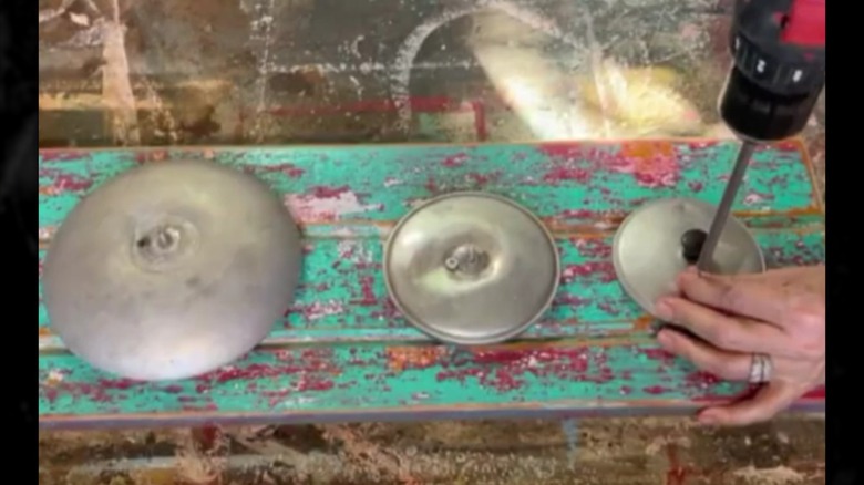 Old lids being drilled onto painted wooden board