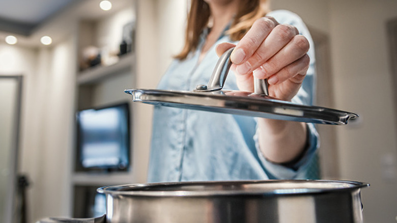A person holding a stainless steel saucepan lid over a pot