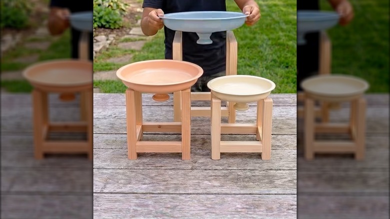 A person adding a painted pot lid to a wooden stand behind two other stands with lids
