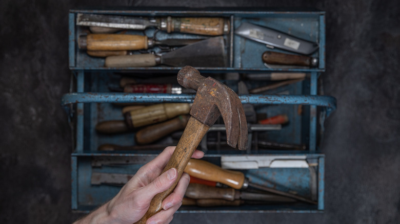 Person holding hammer over old toolbox