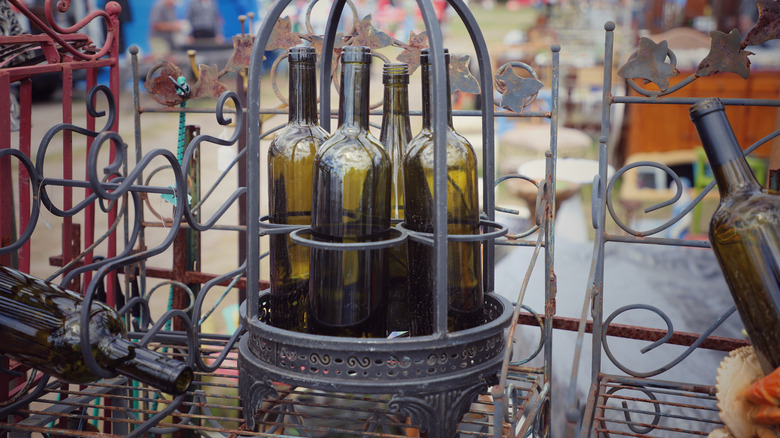 A few old metal wine racks with empty wine bottles inside on display at an outdoor flea market stall.