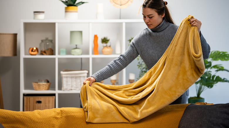 A person drapes multiple blankets on the back of a couch