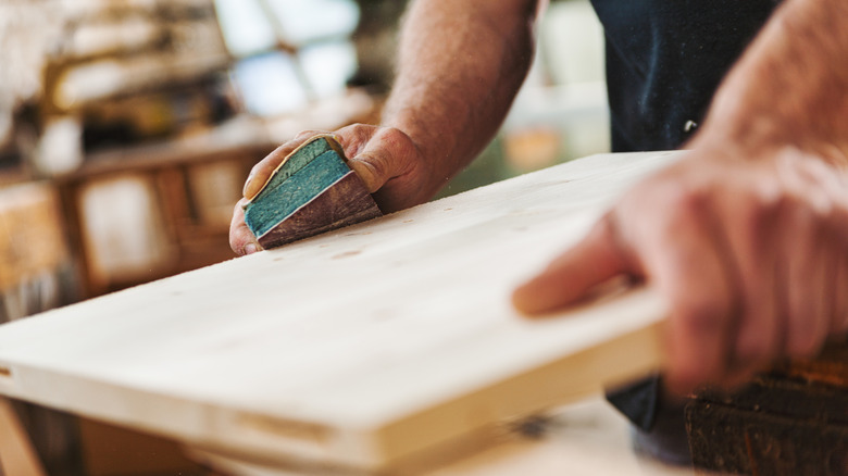 A person manually sands a plank of wood