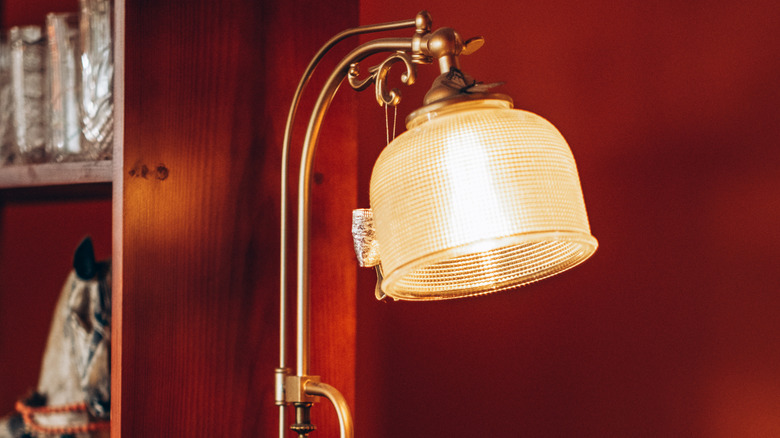 A vintage looking lamp with a yellow tinted glass lampshade on a brass stand with a reddish background.