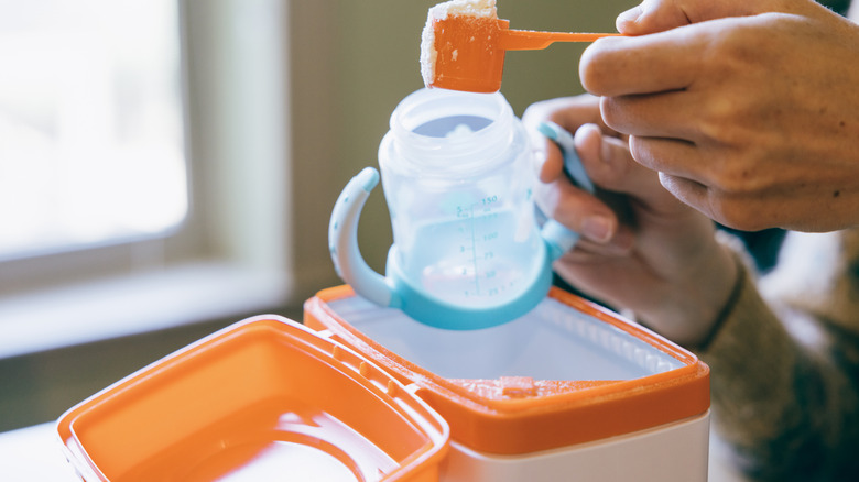 Hands scooping baby formula out of plastic formula container.
