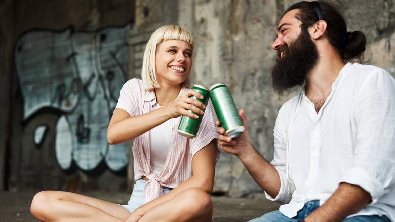 A smiling couple toasts with drinks in cans.