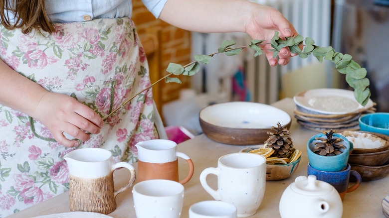 Someone holding a leafy stem over a table with mugs and plates