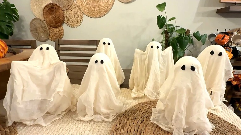 Floating ghosts made out of cheese cloth used as Halloween decor over a table that's covered with a woven tablecloth and woven pot pads