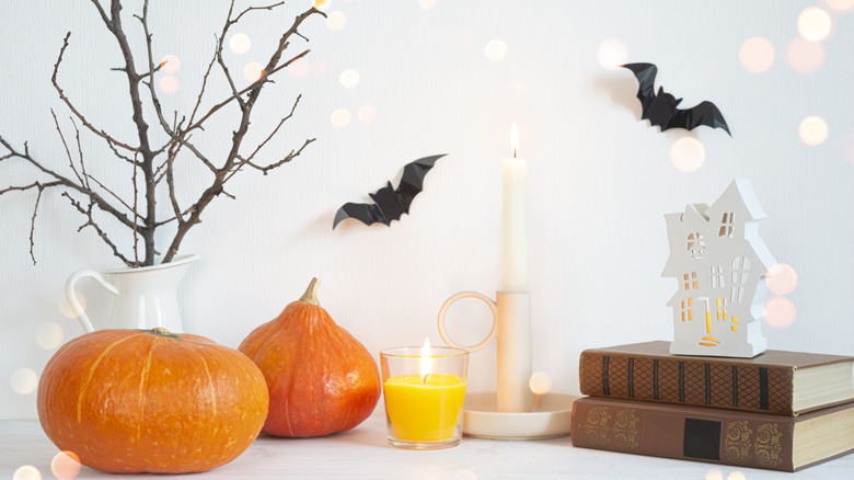 Halloween decor featuring pumpkins, bats, candles, and a ghost house on a stack of books