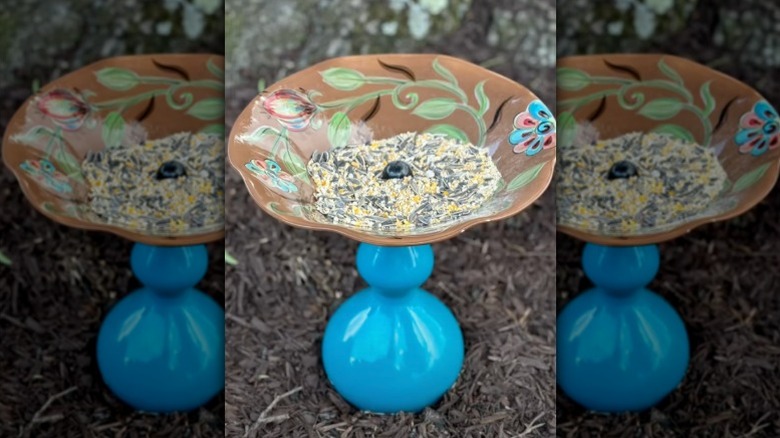A bird feeder filled with seed made from a blue glass lamp base and a decorative platter.