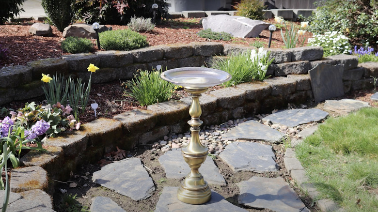 A bird bath made from an ornate gold lamp base and a glass bowl.