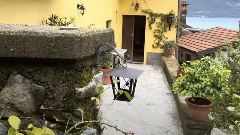 A carriage lantern-style light fixture is repurposed into a bird feeder and hangs on a stone wall in the garden.