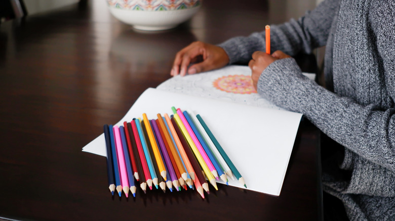 A woman colors a floral design on white paper using colored pencils