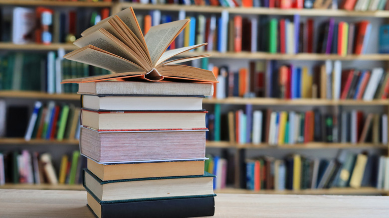 Stack of books on a table in front of book shelf