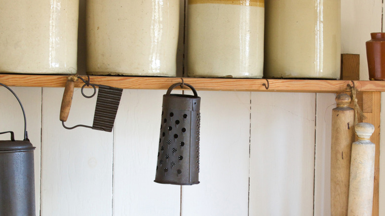 A vintage metal cheese grater hangs from a shelf in an old-fashioned kitchen.
