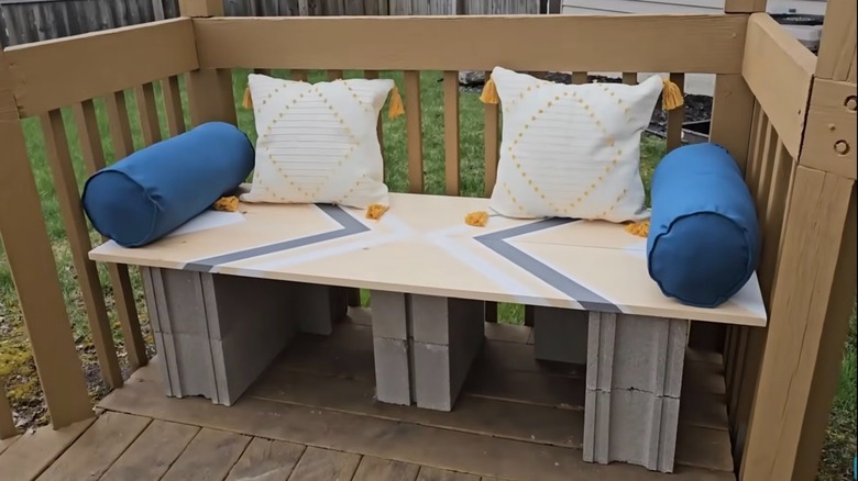 Patio bench made out of cinderblocks and wood planks with decorative pillows.