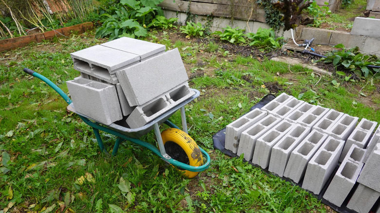 Stacks of cinder blocks on the ground and in a wheelbarrow in the backyard.