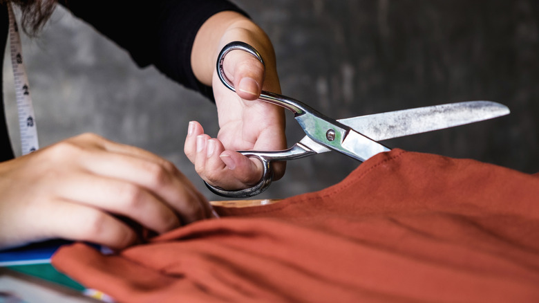 A pair of light-skinned hands cut orange cloth with scissors.
