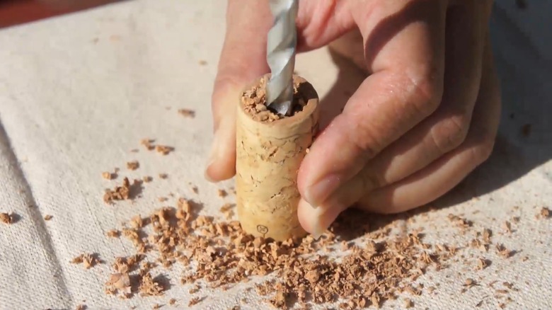 Hands holding a cork and drilling a hole in it